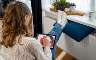 Femme qui dessine sur une tablette avec les pieds sur un radiateur