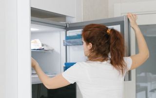 une dame range des denrées dans son congélateur