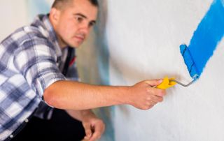 Peintre qui peint un mur en bleu