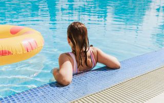 Femme accoudée au bord d'une piscine dans laquelle flotte une bouée